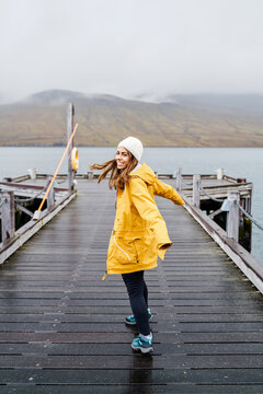 A white woman in a yellow rain jacket enjoys walking on a wooden pier