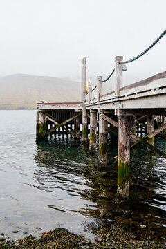 A wooden pier extends over calm sea water with a misty mountain