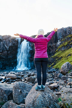 A white woman stands on a rock enjoying a waterfall