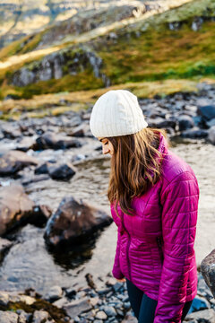 A white woman hikes near a rocky river in Iceland with warm outdoor