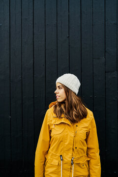 A young white woman in yellow jacket looking sideways by a black