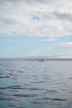 A fishing boat floats on calm waters with snowy hills
