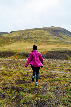 A white person hikes through a grassy mountain landscape