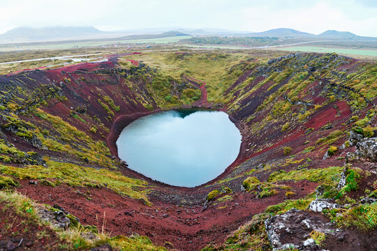 A scenic volcanic crater lake surrounded by red soil and green moss