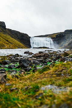 Waterfall flowing into a rocky river with green grass