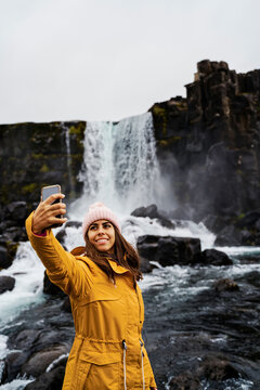 A white woman takes a selfie near a waterfall in Iceland