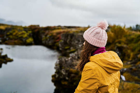 White Woman wearing a yellow jacket looks over a lake