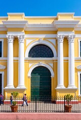 Fototapeta premium Colorful facade of a historic yellow colonial building featuring white columns and a grand green arched door