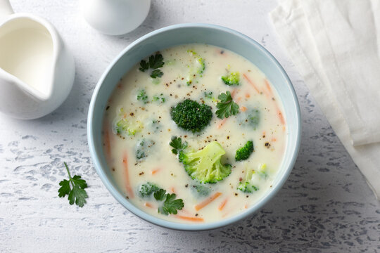 Creamy broccoli soup with potatoes, carrots and herbs in a blue bowl. Homemade vegetable soup with a rich texture on a light background