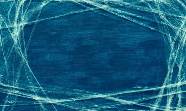 Halloween background with free space for text - white cobweb frame, artificial spider web surrounding center space on the blue painted wooden background
