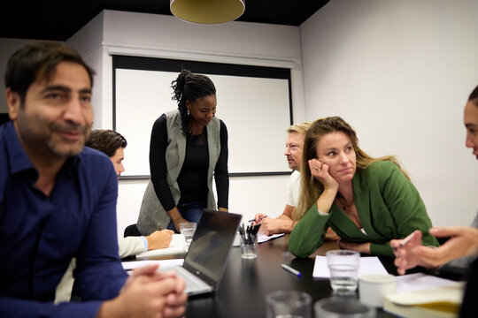 Diverse business professionals sitting around long conference table with laptops and documents