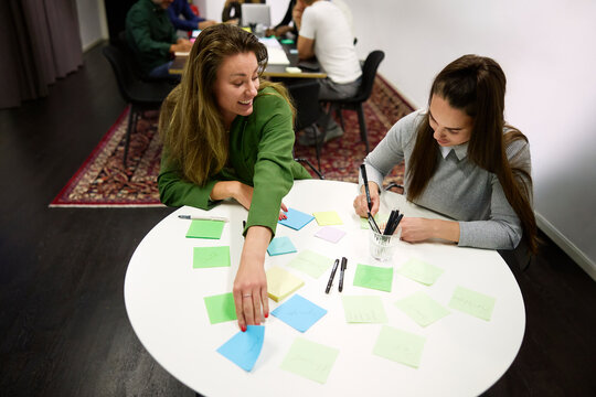 Two female business professionals using colorful sticky notes during brainstorming meeting