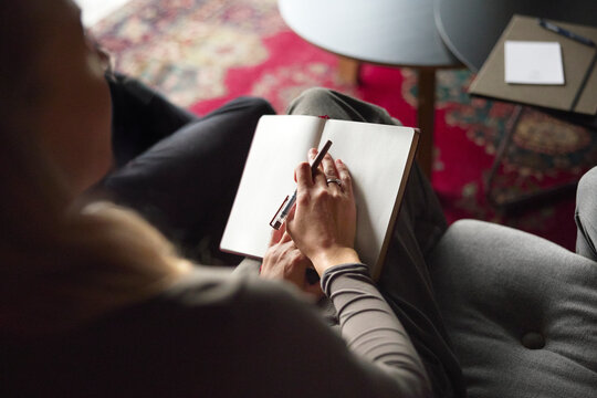Over the shoulder view of businesswoman sitting with diary and pen on sofa
