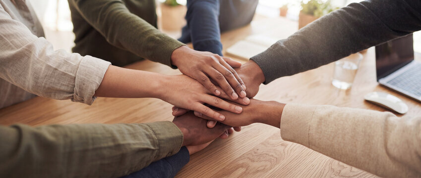 Stacked hands of diverse business team joining together over a wooden meeting desk in office unity, solidarity, and partnership during a collaborative corporate strategy session