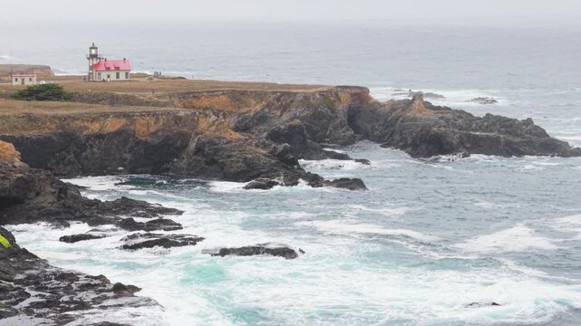 Aerial views showcase Cabrillo Lighthouse and the coastal trail in Mendocino. Fog covers the rugged landscape by the ocean.