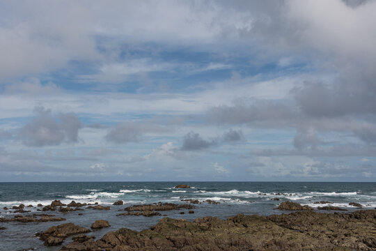 Rough rocky reef coastline with splashing white sea waves under blue sky and clouds in Shingu Wakayama Japan