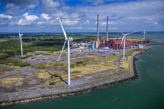 Aerial view of  Moneypoint power station on  Shannon Estuary in County Clare, Ireland with large wind turbines and coastal landscape. Facility transitioning from coal-fired plant into green energy hub