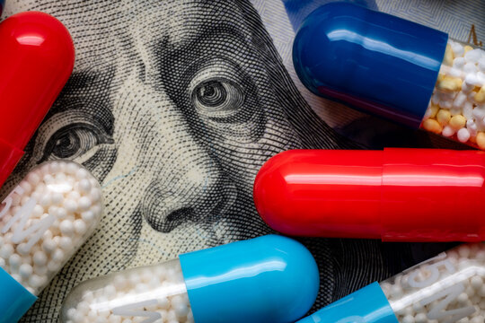 Colorful medicine capsules arranged over Benjamin Franklin on a US 100 dollar bill, representing healthcare costs and pharmaceutical expenses.