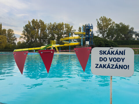 A sign in Czech Republic prohibiting jumping into water at a public swimming pool, water park safety rules, summer holiday setting, outdoor activities.