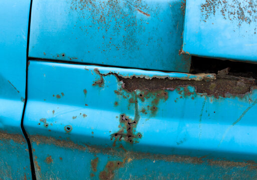 Old blue truck with rust and holes scaring the metal
