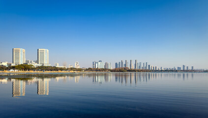 Naklejka premium Serene Waterfront Cityscape with Reflective Skyline Under Clear Blue Sky