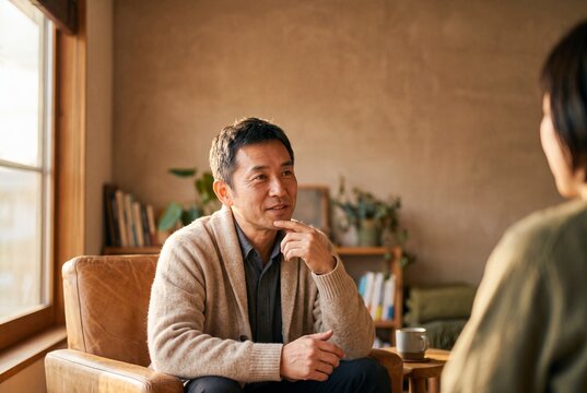 Thoughtful mature Asian man sitting in an armchair listening attentively during a conversation in a cozy room