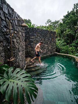 Young Man Stepping into a Luxury Stone Swimming Pool Surrounded by Tropical Jungle Foliage