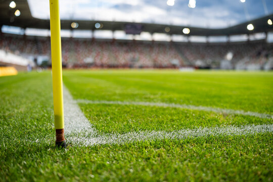 Yellow corner post flag on a professional soccer field with blurred stadium, green grass and spectators in the background during a football match.