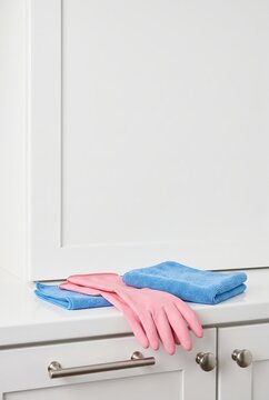 Pink rubber gloves and blue microfiber cloths on white kitchen counter