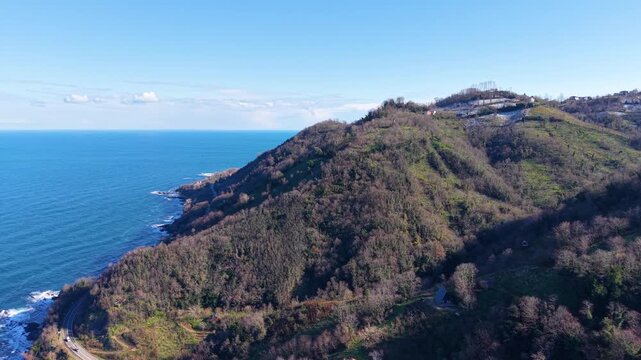Fast cinematic aerial movement from snowy mountain peaks toward the blue sea, combining a smooth right to left pan with forward motion over a scenic coastal landscape.