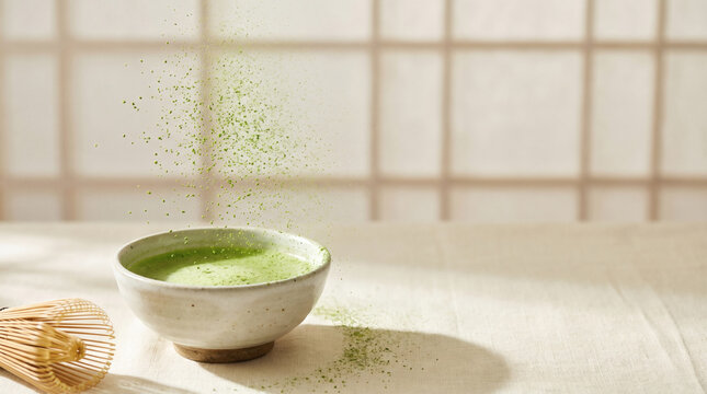 Traditional Japanese matcha green tea in ceramic bowl with falling fine powder and bamboo whisk on linen table in bright zen room