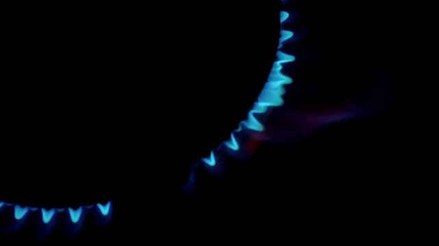 Close-up of a blue gas stove burner flame flickers in the dark. Ideal for energy, cooking, or home concept. Shot with a dark, dramatic low-angle perspective