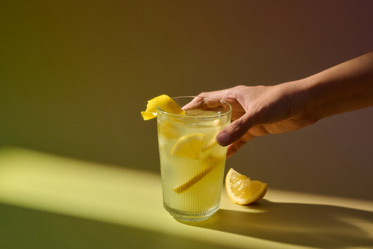 A hand holding a glass of refreshing lemonade with lemon slices