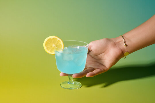 Hand presenting a refreshing blue cocktail with a lemon slice