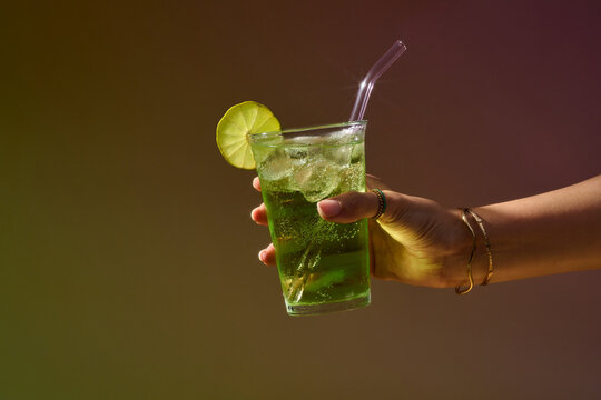 A hand gracefully holds a vibrant green cocktail