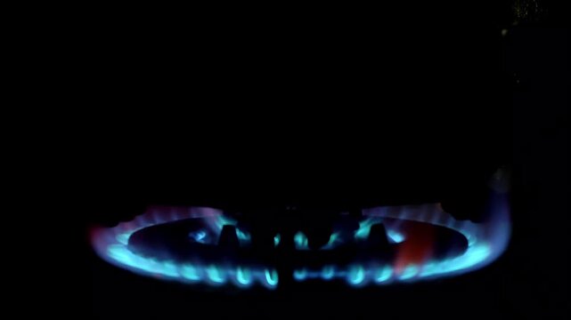 Close-up of a blue gas stove burner flame flickers in the dark. Ideal for energy, cooking, or home concept. Shot with a dark, dramatic low-angle perspective