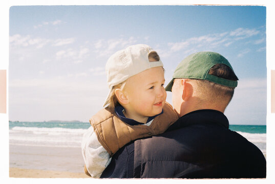 Dad holding toddler on a sandy beach by the sea