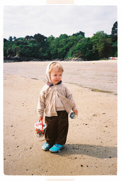 Child holding a bucket of seashells on a quiet beach