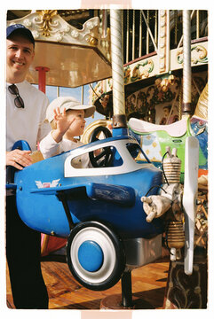 Toddler riding a carousel airplane with father nearby