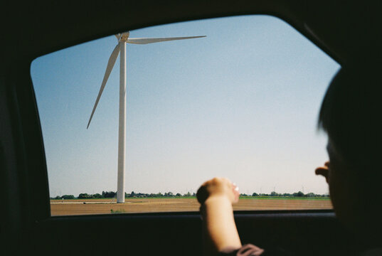 Unrecognizable child watching a wind turbine from a car