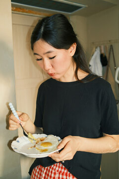 Young beautiful asian woman eating a fried egg for morning breakfast 