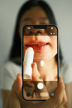 Smartphone screen showing close up of asian woman applying lip balm