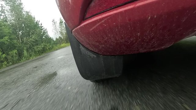 Dynamic View of a Wet Road with a Focus on a Red Vehicle's Rear Tire and Spray, Capturing the Motion and Ambiance of Rainy Driving Conditions