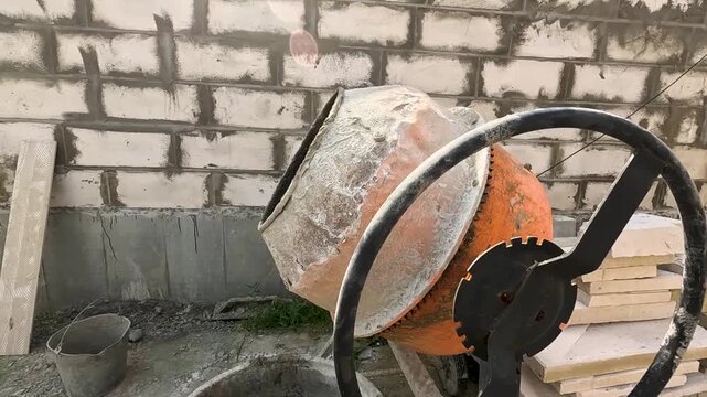 Construction Site Featuring a Concrete Mixer Machine and Various Building Materials Along a Brick Wall, Illustrating the Process of Mixing Concrete for Construction Projects
