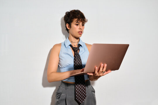 Professional woman using laptop. A woman in a blue shirt and tie holds a laptop. She looks focused, typing or reviewing content. Her expression