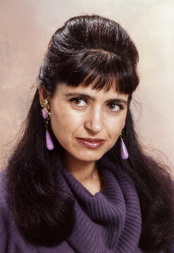 Woman with dark hair wearing purple sweater and earrings
