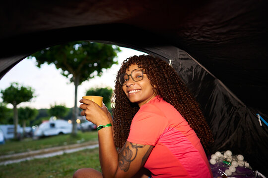 Woman enjoying drink while relaxing at campsite tent
