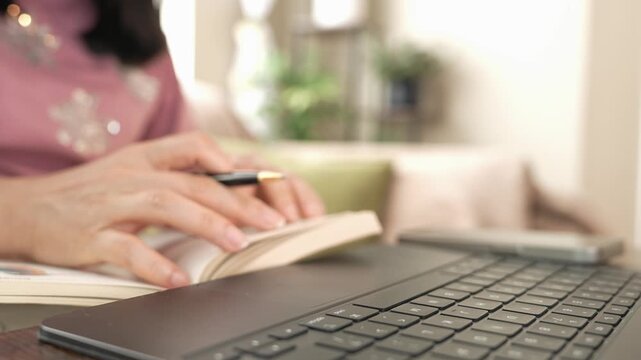 Woman reading a book, checking laptop screen, typing and using smartphone at home for research, online learning, career development, professional growth, training and modern work skills.