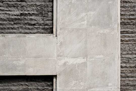 Modern architectural wall texture featuring interlocking light grey concrete panels and rough dark grey stacked stone veneer. Abstract geometric exterior building facade background.
