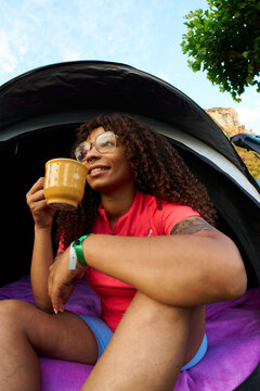 Woman enjoying morning coffee at campsite opening tent